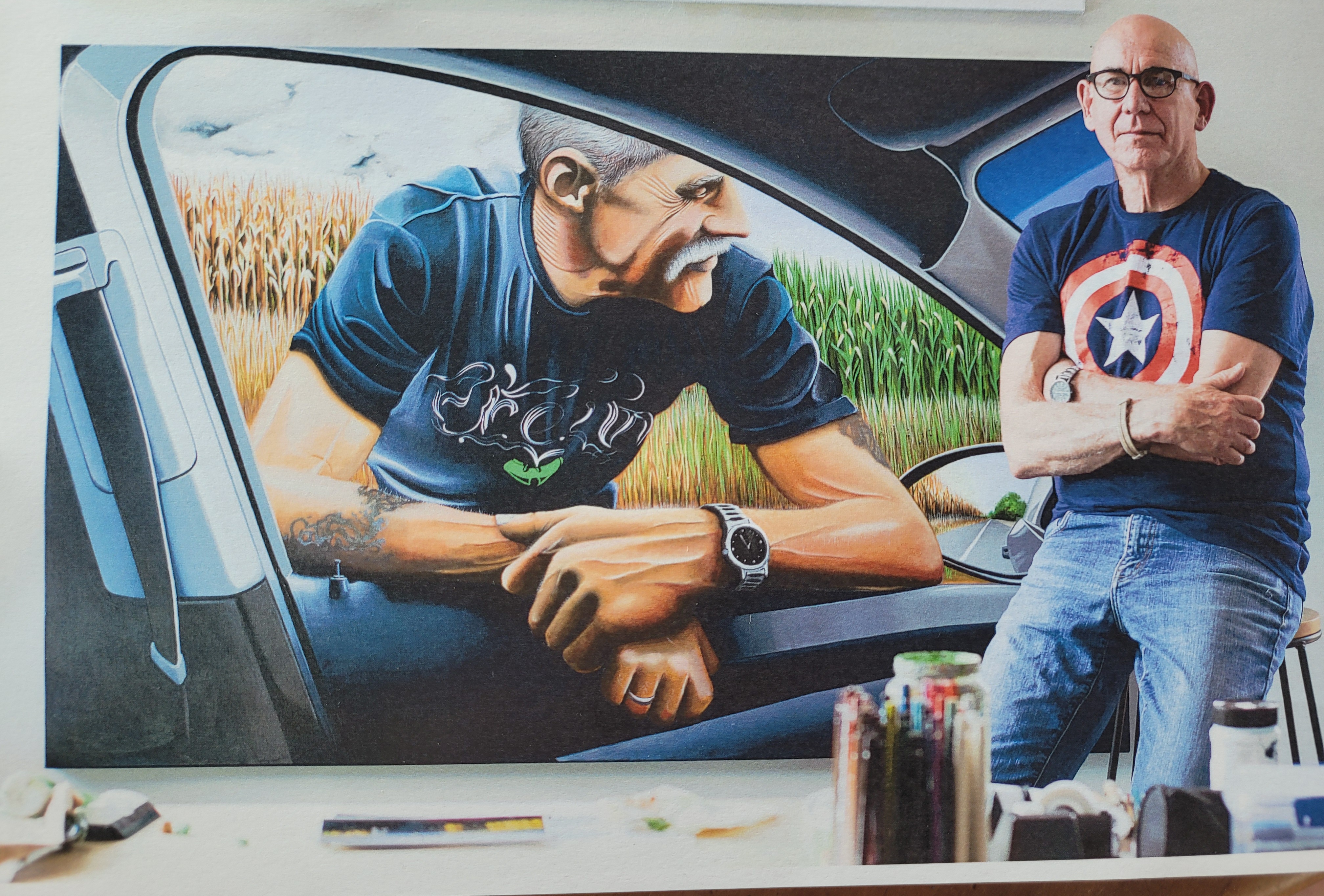 David Jung seated beside a large painting of Tony leaning through a car window